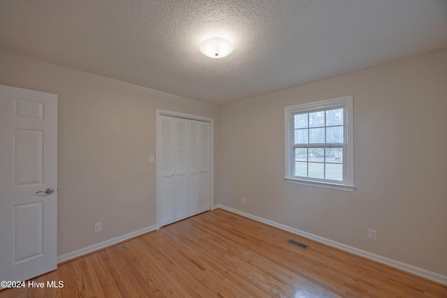 unfurnished bedroom with a closet, a textured ceiling, and light hardwood / wood-style flooring