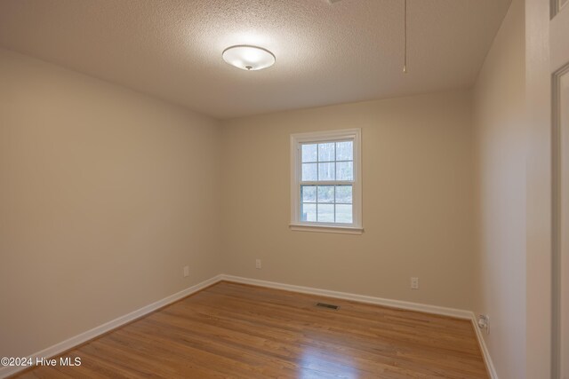 spare room with a textured ceiling and light hardwood / wood-style flooring