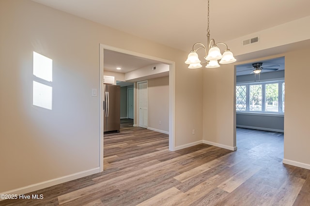 unfurnished dining area with ceiling fan with notable chandelier and hardwood / wood-style flooring