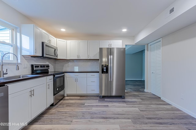 kitchen featuring sink, light hardwood / wood-style flooring, backsplash, white cabinets, and appliances with stainless steel finishes