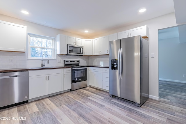 kitchen featuring decorative backsplash, stainless steel appliances, sink, light hardwood / wood-style floors, and white cabinetry