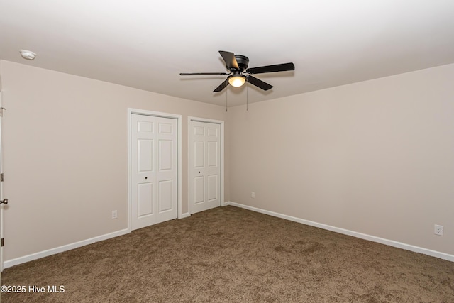 unfurnished bedroom featuring dark colored carpet, two closets, and ceiling fan