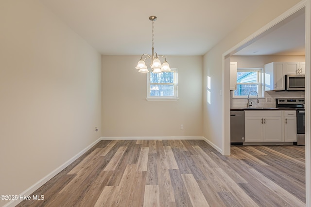 unfurnished dining area with sink, a chandelier, and light wood-type flooring