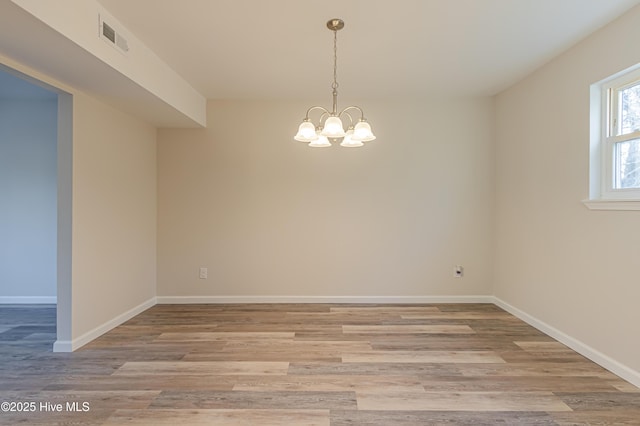 spare room featuring light wood-type flooring and an inviting chandelier