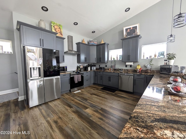 kitchen with pendant lighting, lofted ceiling, wall chimney exhaust hood, gray cabinets, and stainless steel appliances