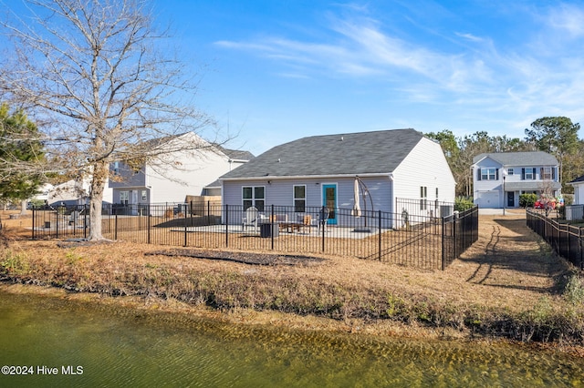 back of house featuring a patio area, a water view, roof with shingles, and fence