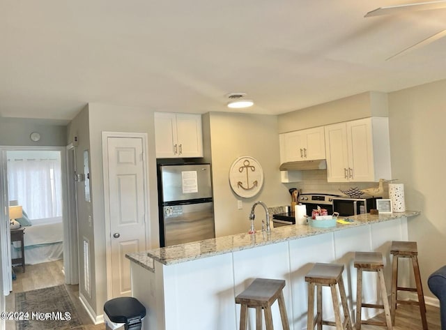 kitchen featuring white cabinets, decorative backsplash, light stone countertops, kitchen peninsula, and stainless steel appliances