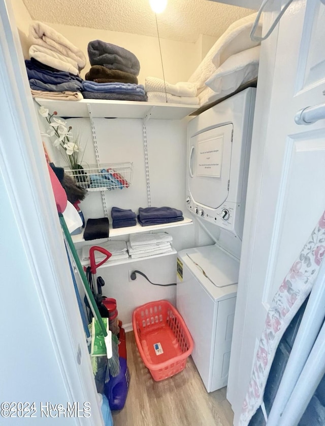 laundry area featuring stacked washer and dryer, light hardwood / wood-style floors, and a textured ceiling