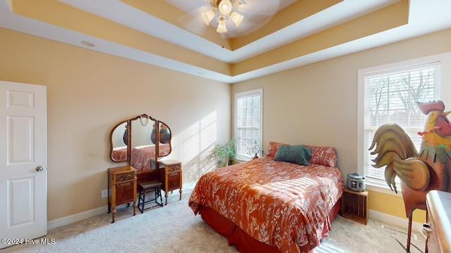 bedroom with light carpet, a raised ceiling, and ceiling fan