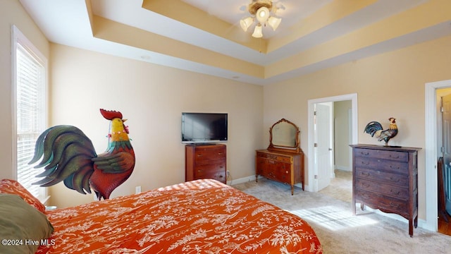 bedroom with light carpet, a tray ceiling, and ceiling fan