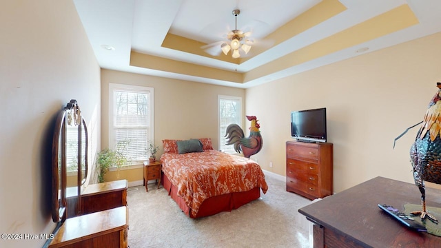 carpeted bedroom featuring multiple windows, a tray ceiling, and ceiling fan