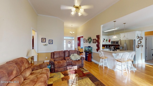 living room with ceiling fan with notable chandelier, light wood-type flooring, and crown molding