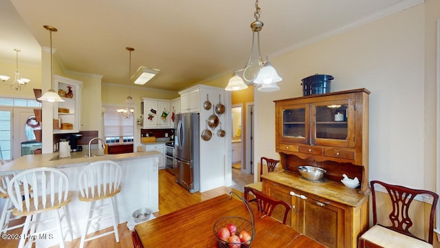 dining space featuring light hardwood / wood-style flooring, ornamental molding, sink, and an inviting chandelier