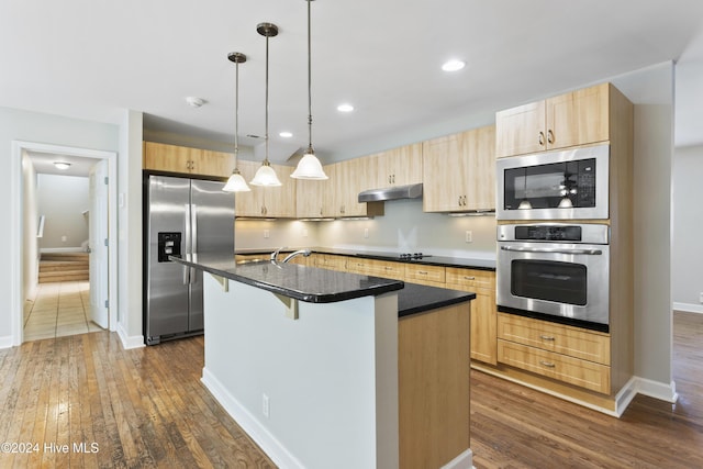 kitchen with pendant lighting, dark wood-type flooring, a center island with sink, light brown cabinetry, and stainless steel appliances