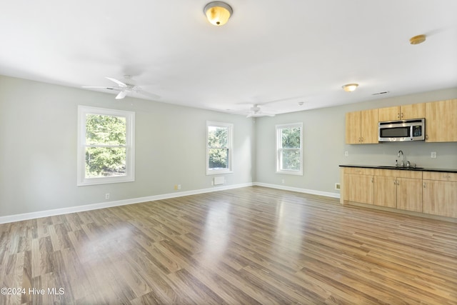 unfurnished living room featuring plenty of natural light, ceiling fan, light wood-type flooring, and sink