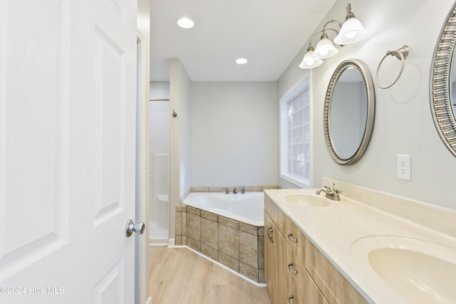 bathroom with wood-type flooring, vanity, and tiled bath