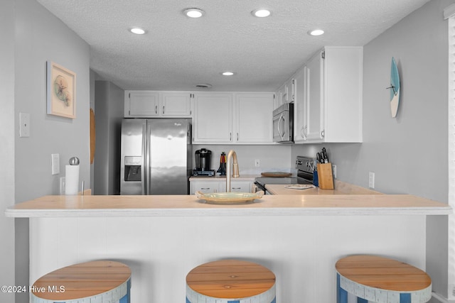 kitchen with kitchen peninsula, appliances with stainless steel finishes, a kitchen bar, a textured ceiling, and white cabinets