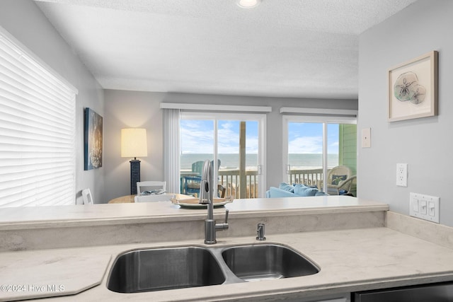 kitchen with a textured ceiling, a water view, stainless steel dishwasher, and sink