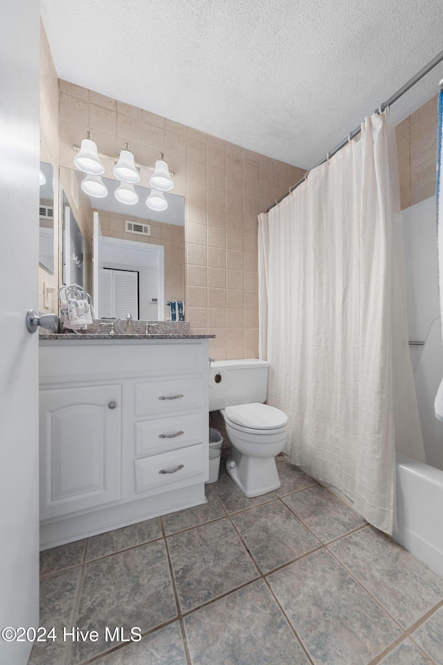 full bathroom with vanity, shower / bath combination with curtain, toilet, a textured ceiling, and tile walls