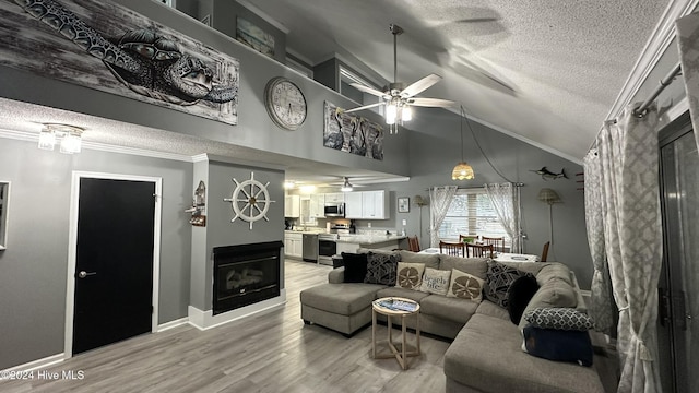 living room with ceiling fan, crown molding, hardwood / wood-style floors, a textured ceiling, and lofted ceiling