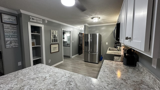 kitchen with stainless steel refrigerator with ice dispenser, a textured ceiling, crown molding, sink, and white cabinets