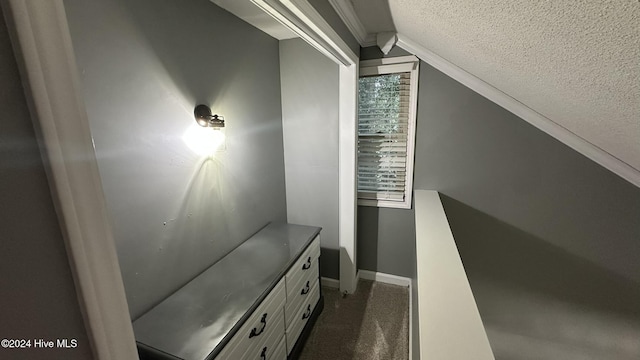 corridor featuring a textured ceiling, dark carpet, and vaulted ceiling