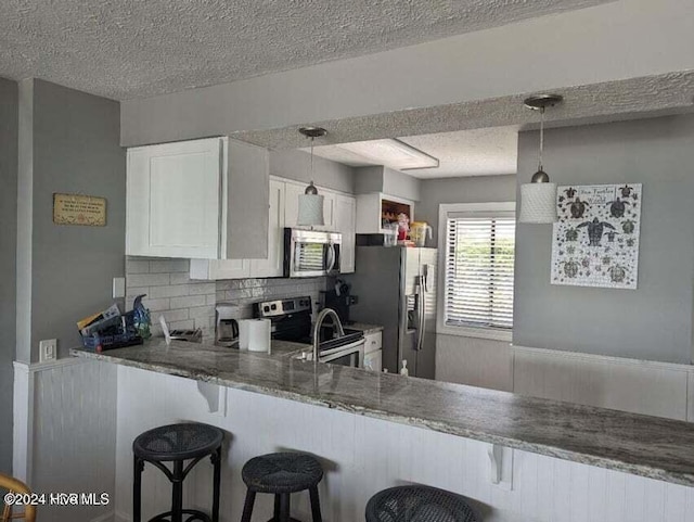 kitchen featuring pendant lighting, a kitchen breakfast bar, kitchen peninsula, appliances with stainless steel finishes, and white cabinetry