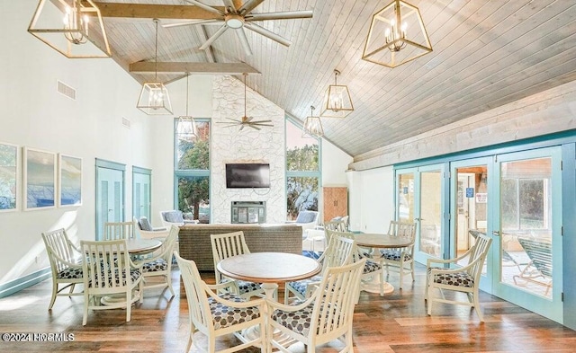 dining area with a stone fireplace, high vaulted ceiling, and wood-type flooring