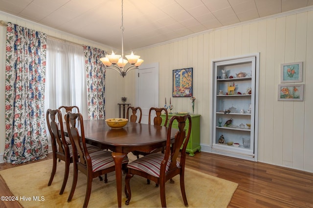 dining space featuring wood-type flooring, built in features, crown molding, and a chandelier