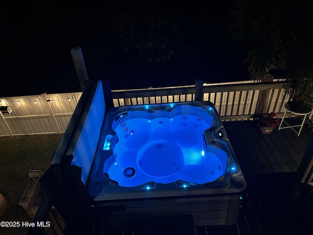 pool at night featuring fence, a wooden deck, and a hot tub
