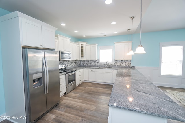 kitchen featuring light stone counters, stainless steel appliances, a sink, a peninsula, and tasteful backsplash