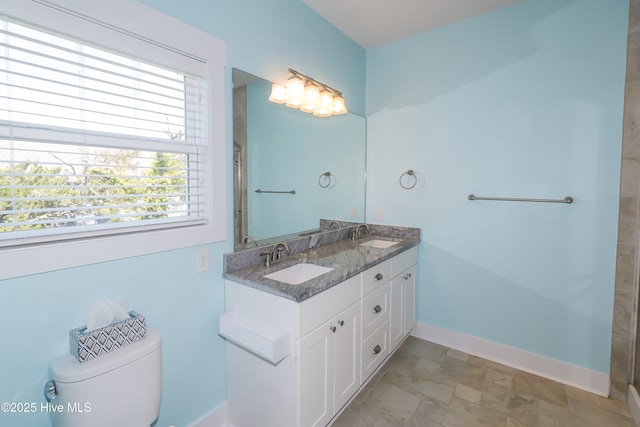 bathroom with baseboards, a sink, double vanity, and toilet