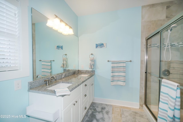 full bathroom featuring baseboards, double vanity, a stall shower, and a sink