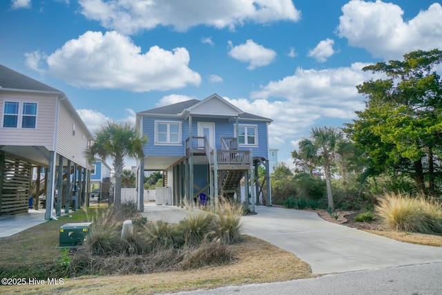 coastal home featuring concrete driveway, a carport, stairs, and covered porch