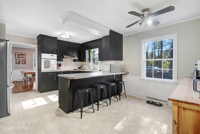 kitchen featuring kitchen peninsula, ceiling fan, a breakfast bar area, oven, and stainless steel refrigerator