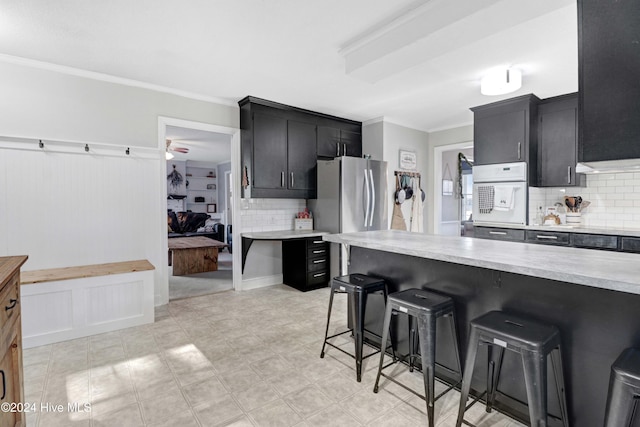 kitchen featuring stainless steel refrigerator, white oven, a kitchen breakfast bar, crown molding, and decorative backsplash