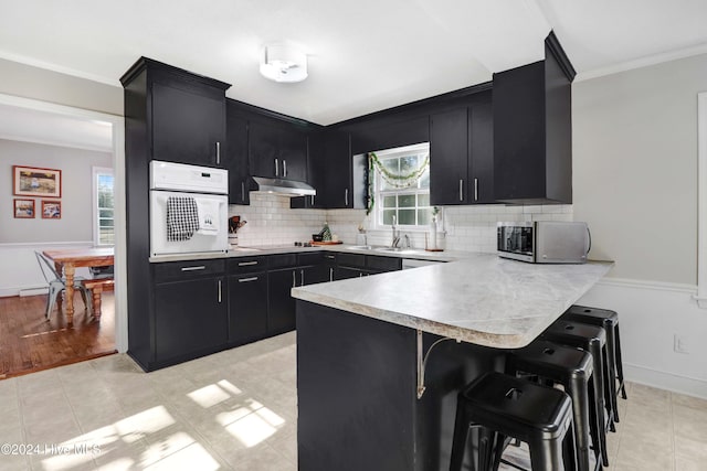 kitchen featuring white oven, sink, ornamental molding, a kitchen bar, and kitchen peninsula