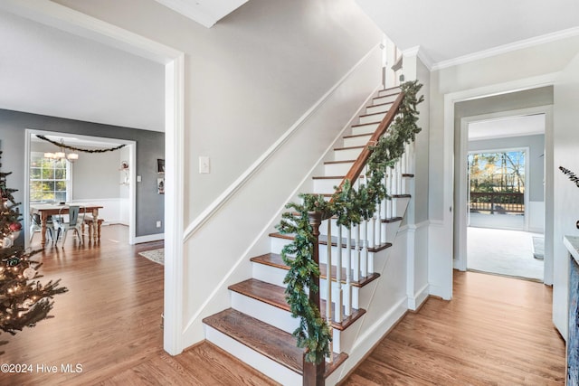 stairway featuring hardwood / wood-style flooring, ornamental molding, and a notable chandelier