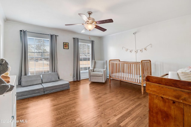 bedroom with ceiling fan, hardwood / wood-style floors, crown molding, and a crib