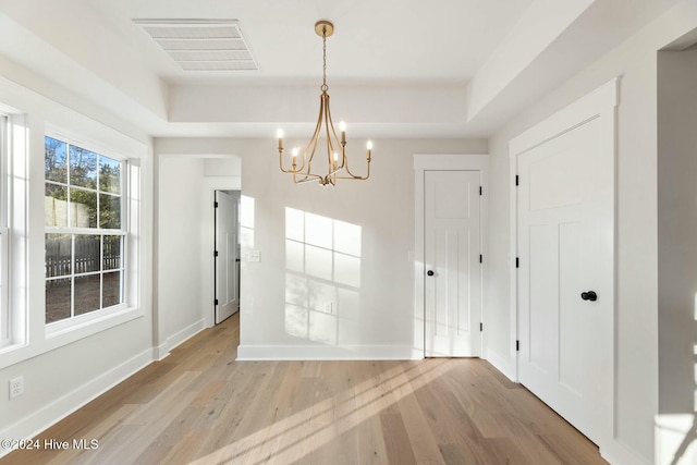 unfurnished dining area with light hardwood / wood-style floors, a raised ceiling, and an inviting chandelier