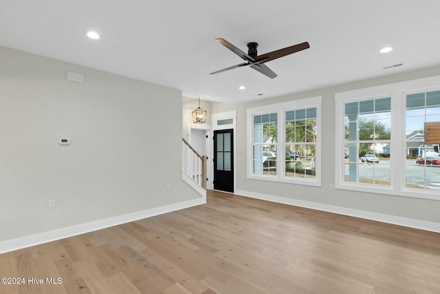 spare room with ceiling fan with notable chandelier and light wood-type flooring