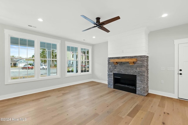 unfurnished living room featuring a stone fireplace, ceiling fan, and light hardwood / wood-style floors