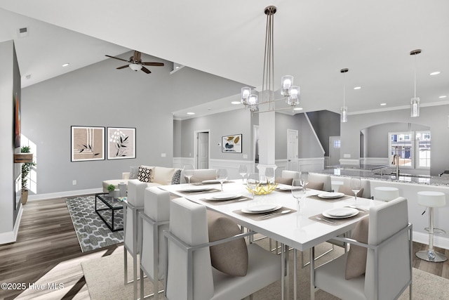 dining space with hardwood / wood-style floors, high vaulted ceiling, ceiling fan with notable chandelier, and ornamental molding