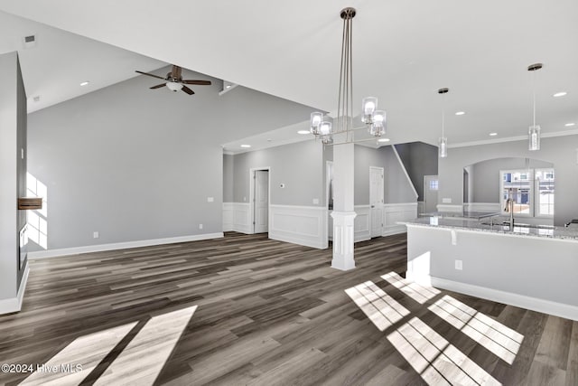 unfurnished living room with ornate columns, dark wood-type flooring, vaulted ceiling, ceiling fan with notable chandelier, and ornamental molding