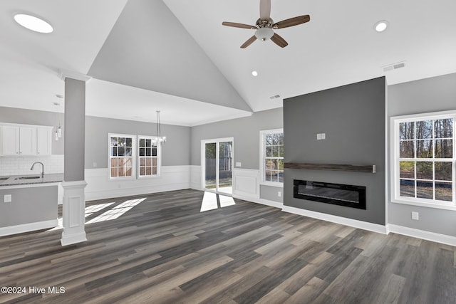 unfurnished living room with ceiling fan with notable chandelier, high vaulted ceiling, dark wood-type flooring, and sink