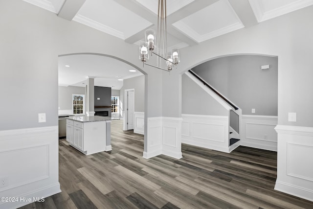 unfurnished dining area featuring dark wood-type flooring, an inviting chandelier, coffered ceiling, crown molding, and beam ceiling