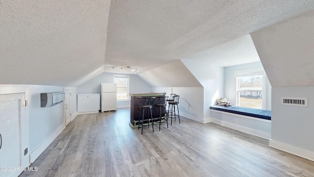 additional living space with a textured ceiling, bar, light hardwood / wood-style floors, and vaulted ceiling