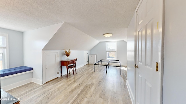 recreation room featuring a textured ceiling, light wood-type flooring, and vaulted ceiling