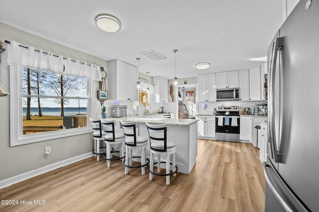 kitchen with light stone countertops, white cabinetry, hanging light fixtures, stainless steel appliances, and a breakfast bar