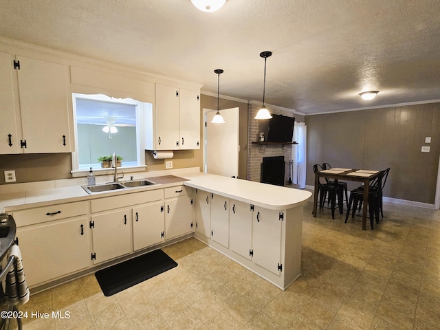 kitchen featuring kitchen peninsula, a brick fireplace, a textured ceiling, sink, and decorative light fixtures